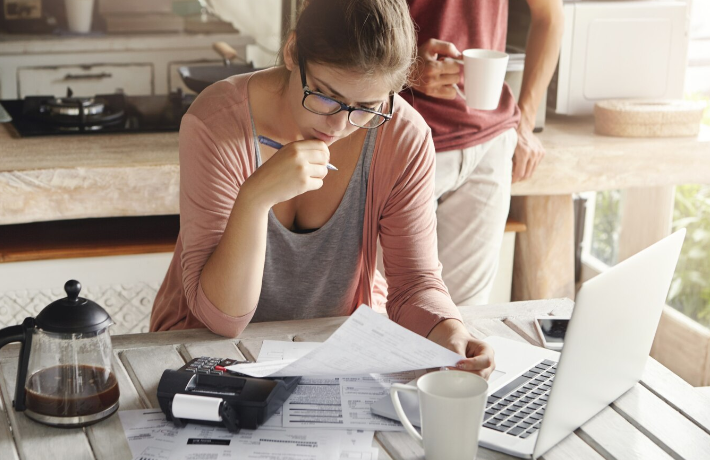 Jolie femme à lunettes ayant un regard sérieux et concentré tenant un stylo tout en remplissant des papiers, en calculant les factures, en réduisant les dépenses familiales, en essayant d'économiser de l'argent pour faire de gros achats